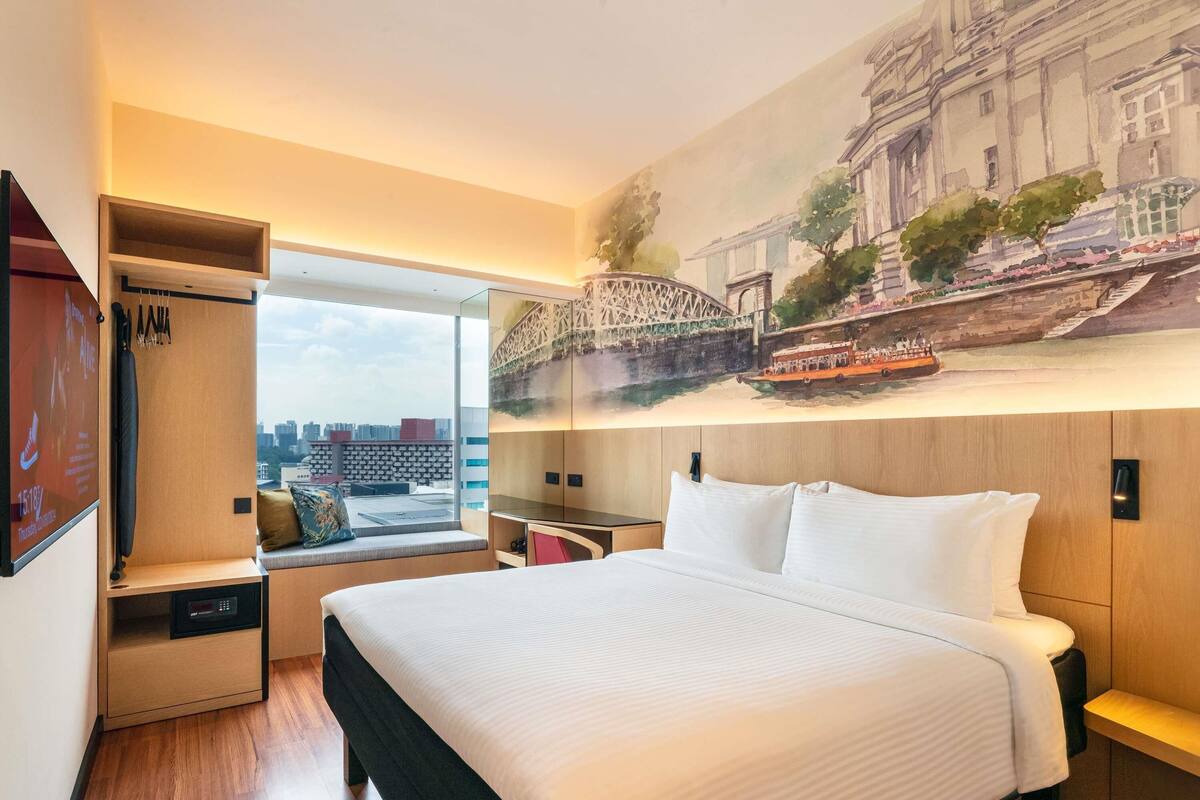 Una habitación de hotel con una cama grande, zona de estar con vistas, armario y un mural de un puente.