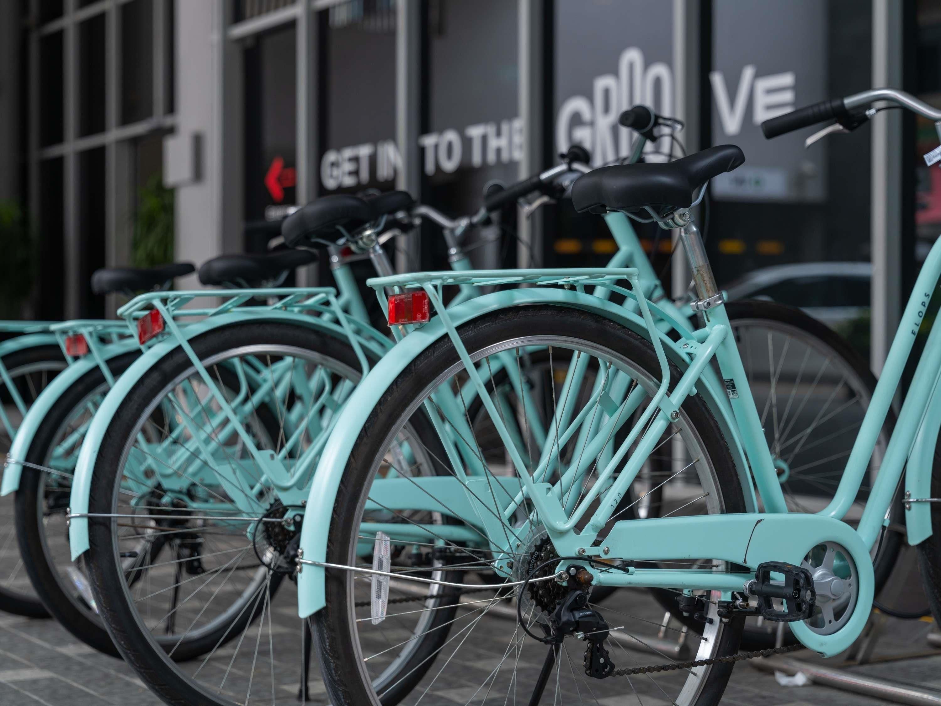 A row of turquoise bicycles parked in front of a building with a sign that reads 'Get in to the GRIOVE.'