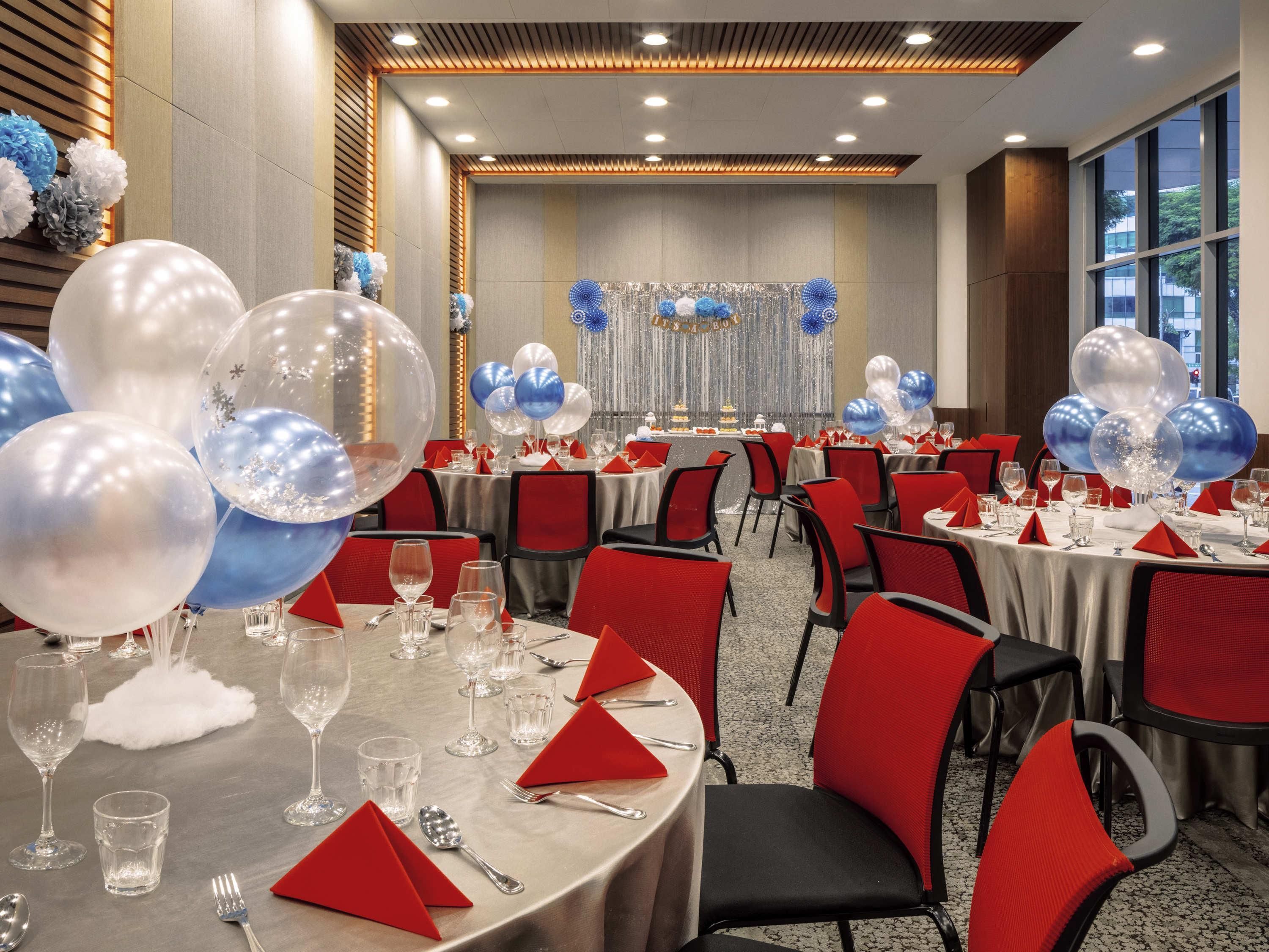 Un salón de banquetes con mesas redondas, sillas rojas y globos.