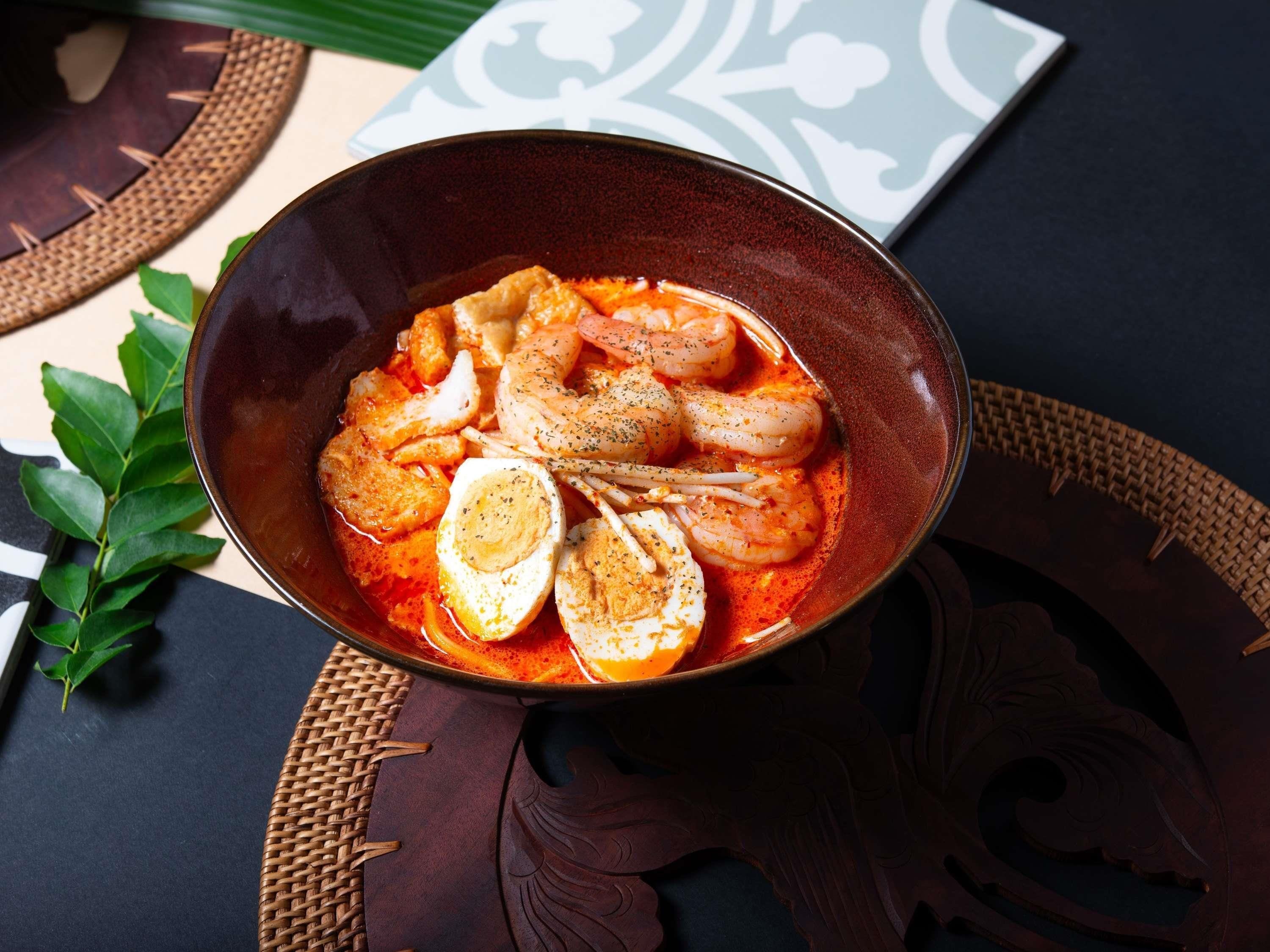 A bowl of food with shrimp and eggs on a dark surface.