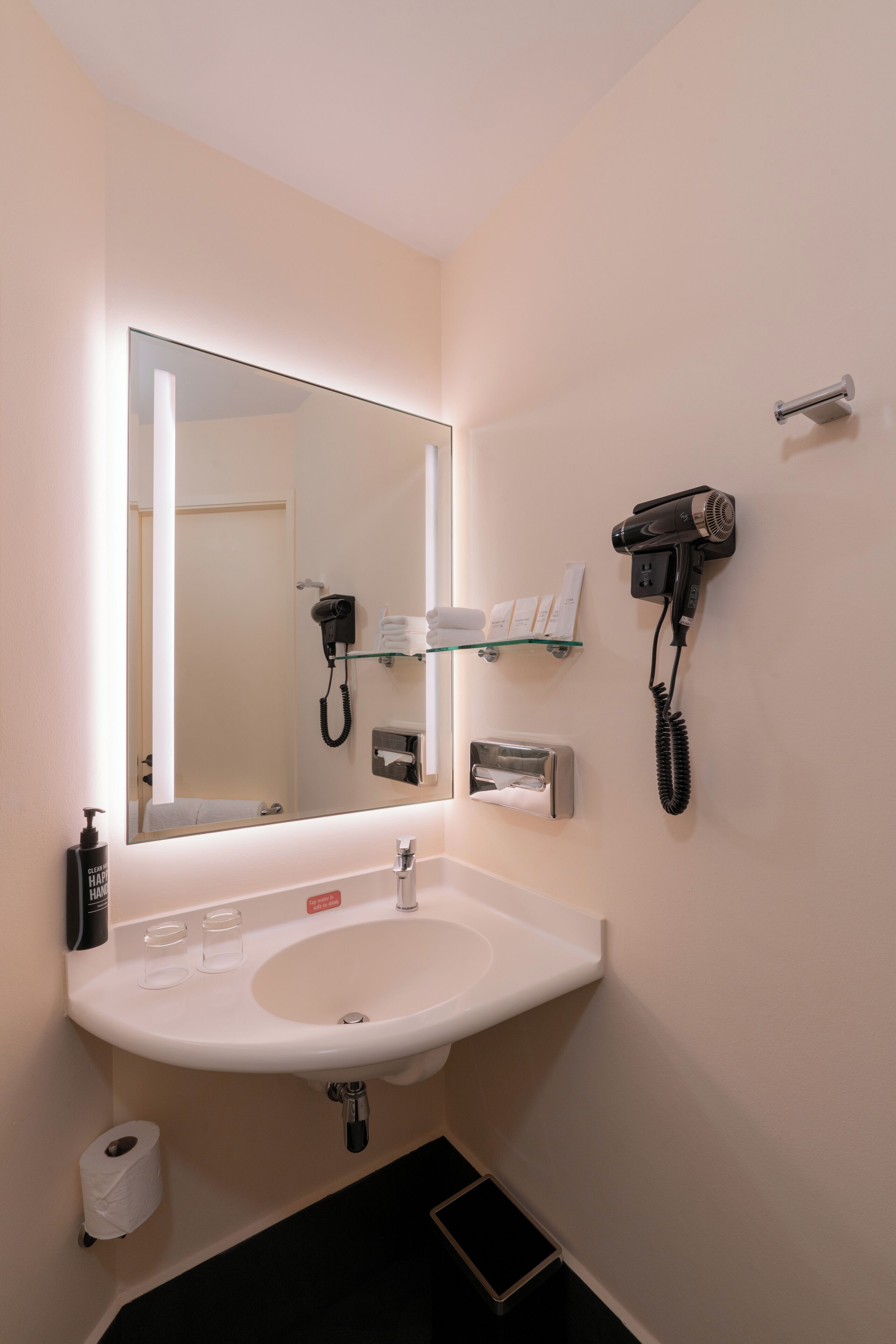 A bathroom with a sink, mirror, hairdryer, and a shelf with toiletries.