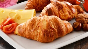 En morgenmads tallerken med croissanter, ost, tomater og et udvalg af frugt og juicer.