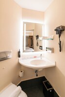 Un baño con lavamanos blanco, espejo, secador de pelo y toallero.