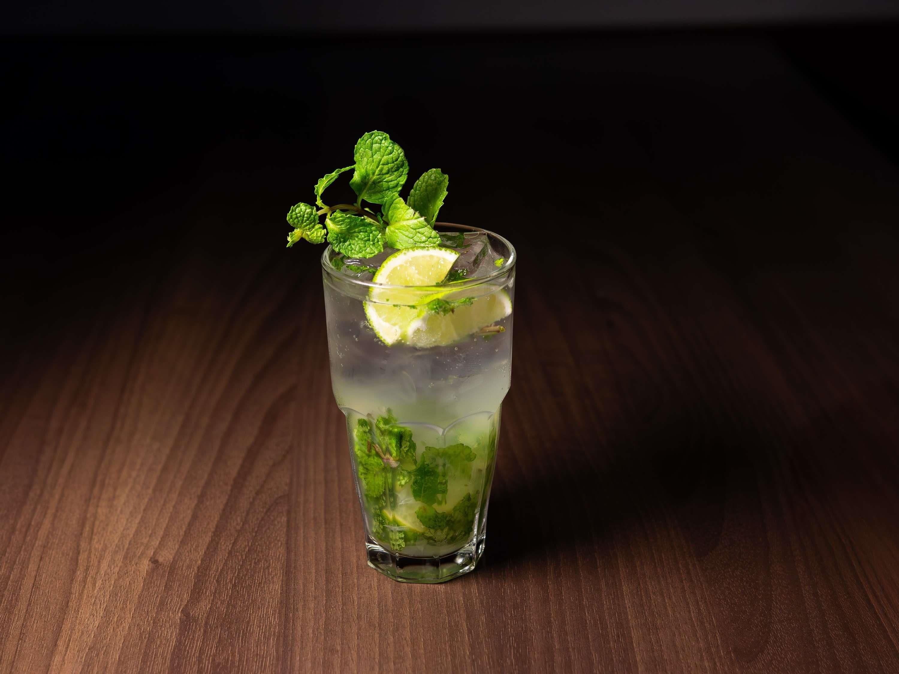 A glass of a clear beverage with lime and mint garnish on a wooden surface.