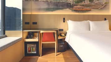 A hotel room with a bed, a desk with a chair, a small cabinet, and a window.