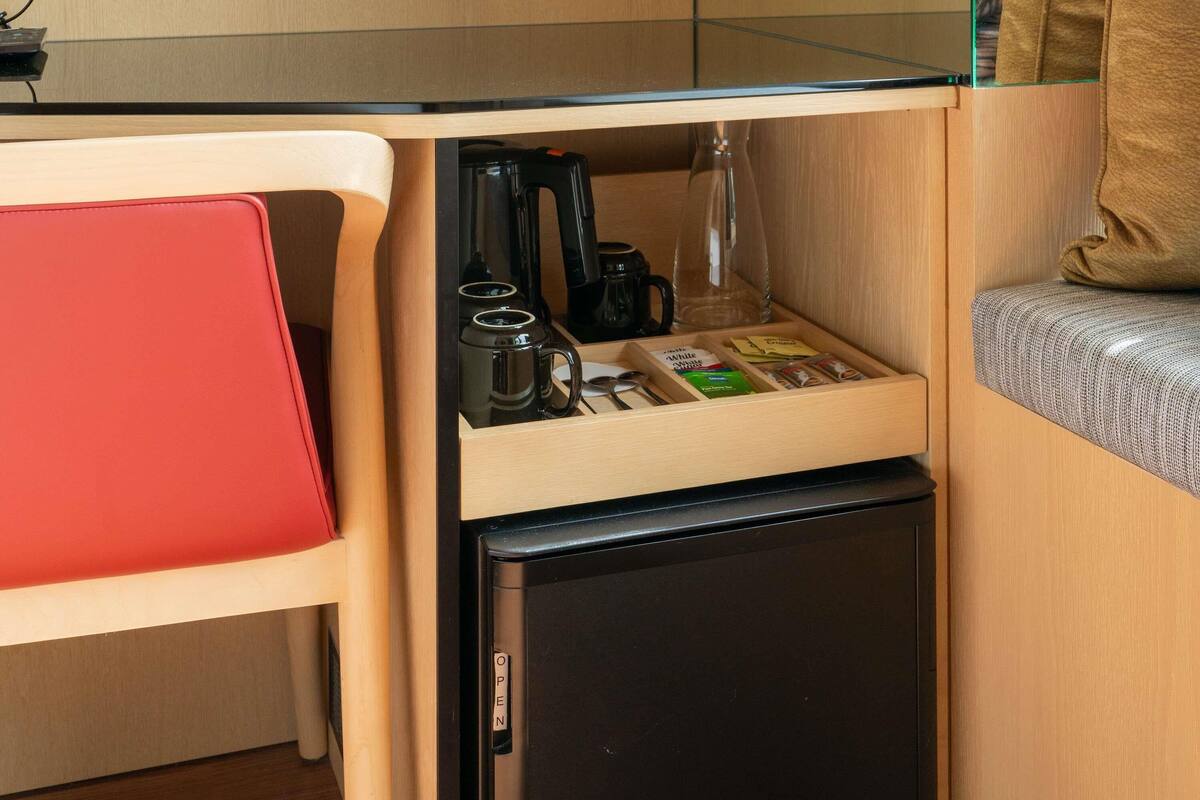 A compact kitchenette with a coffee maker, mugs, and a small fridge.