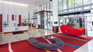 Un vestíbulo moderno con un mostrador de recepción, un sofá rojo, un banco gris y ventanas amplias que ofrecen vistas al exterior.