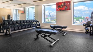 Un gimnasio con mancuernas, bancos y vistas a la ciudad.