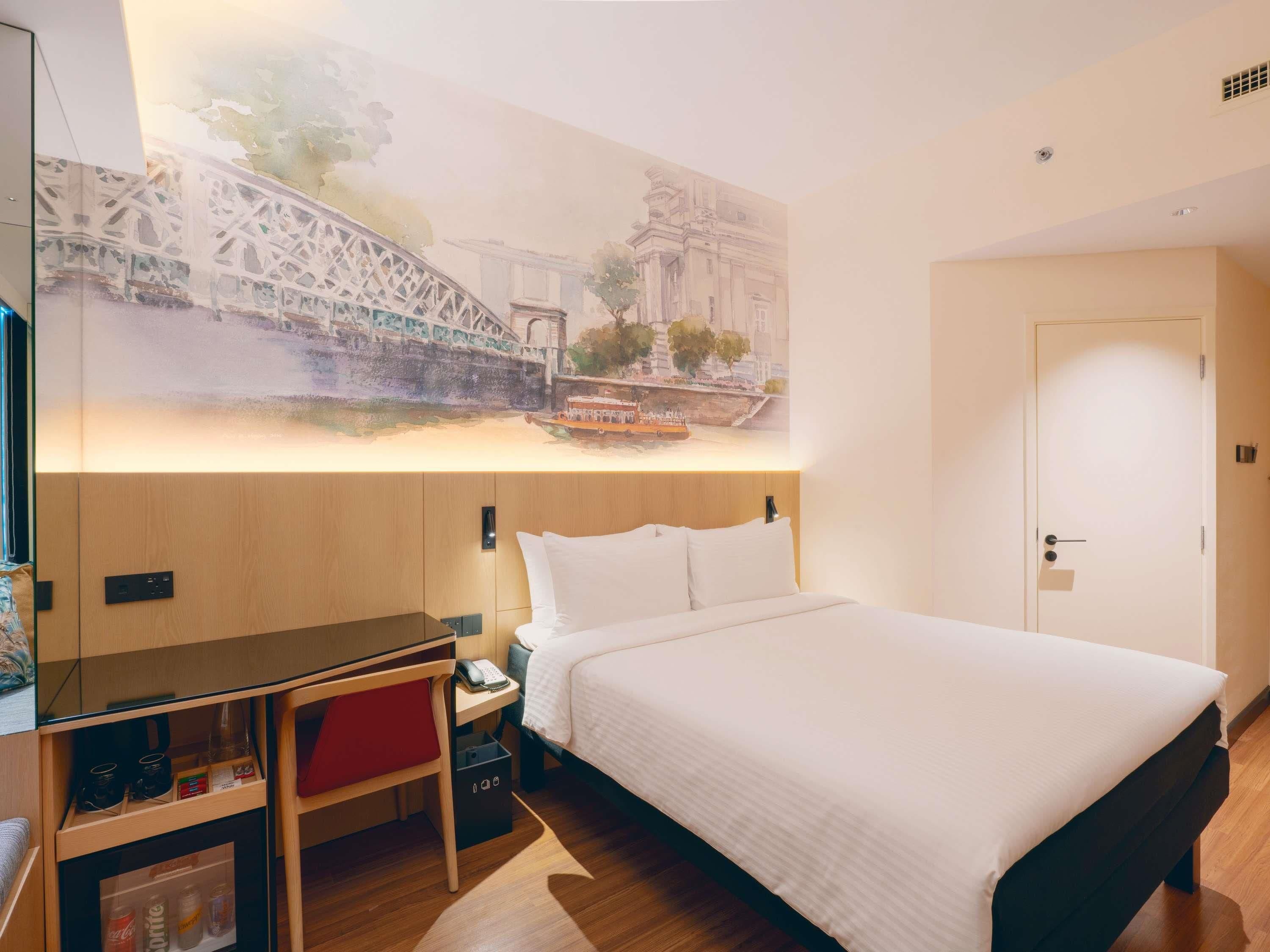 A hotel room with a bed, a desk, a chair, a phone, a small cabinet, and a wall-mounted artwork.
