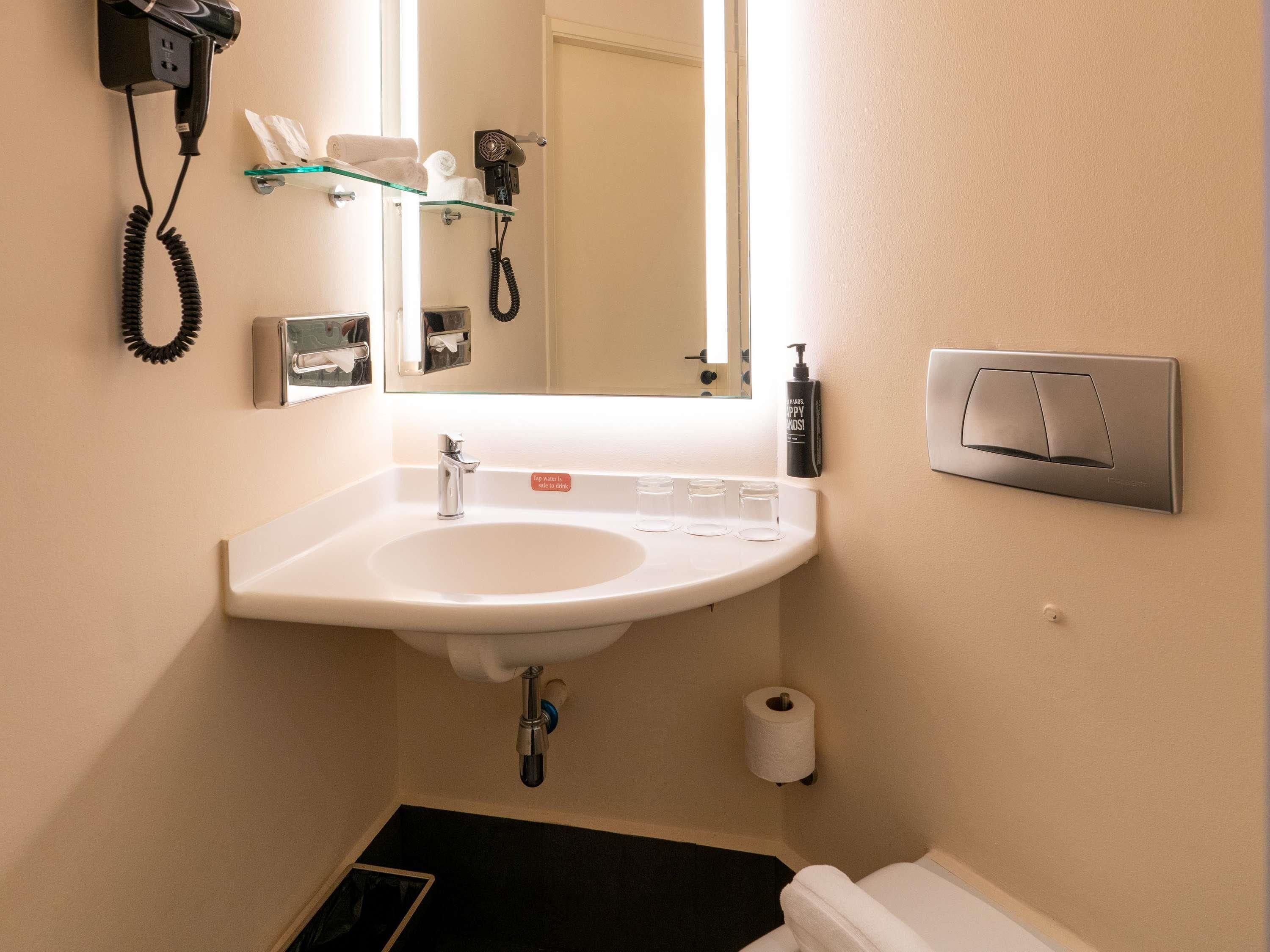 A bathroom with a sink, mirror, towel rack, hairdryer, and toilet paper.