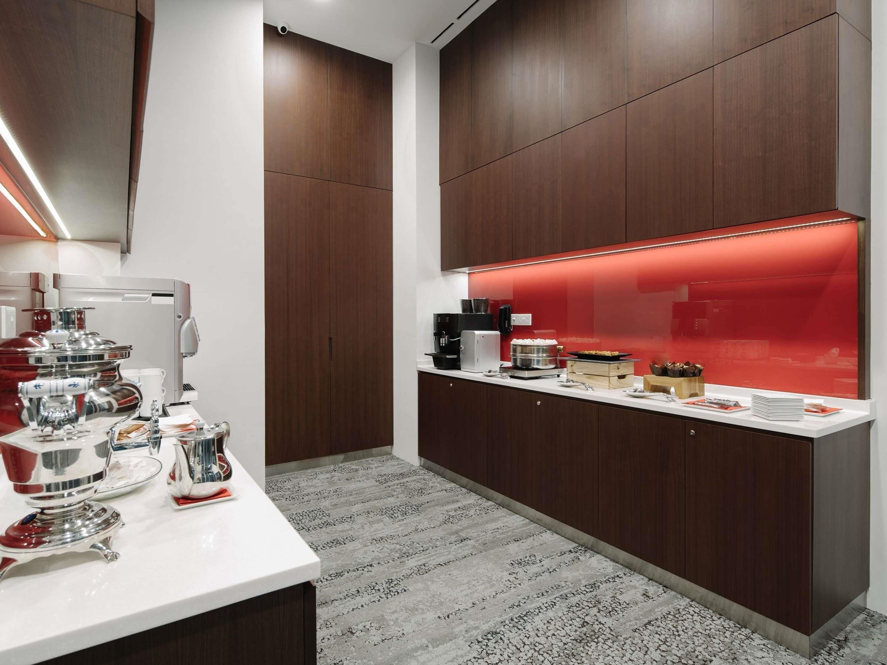Una cocina moderna con encimera blanca, electrodomésticos de acero inoxidable y una vitrina iluminada con luz roja.