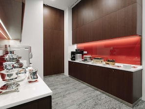 Una cocina moderna con encimera blanca, electrodomésticos de acero inoxidable y una vitrina iluminada con luz roja.