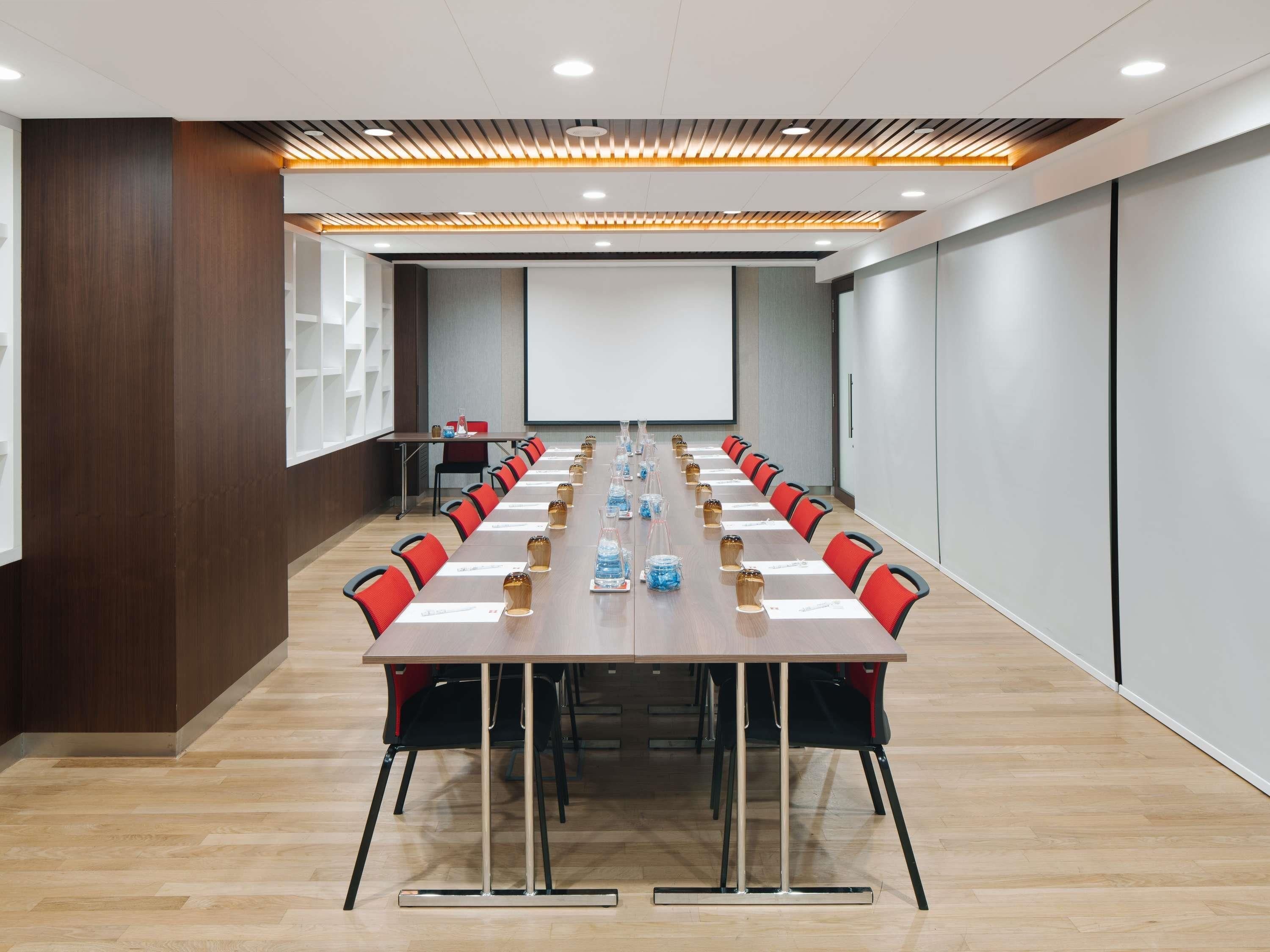 Un salón de conferencias con una larga mesa, sillas, una pantalla de proyector y una pizarra.