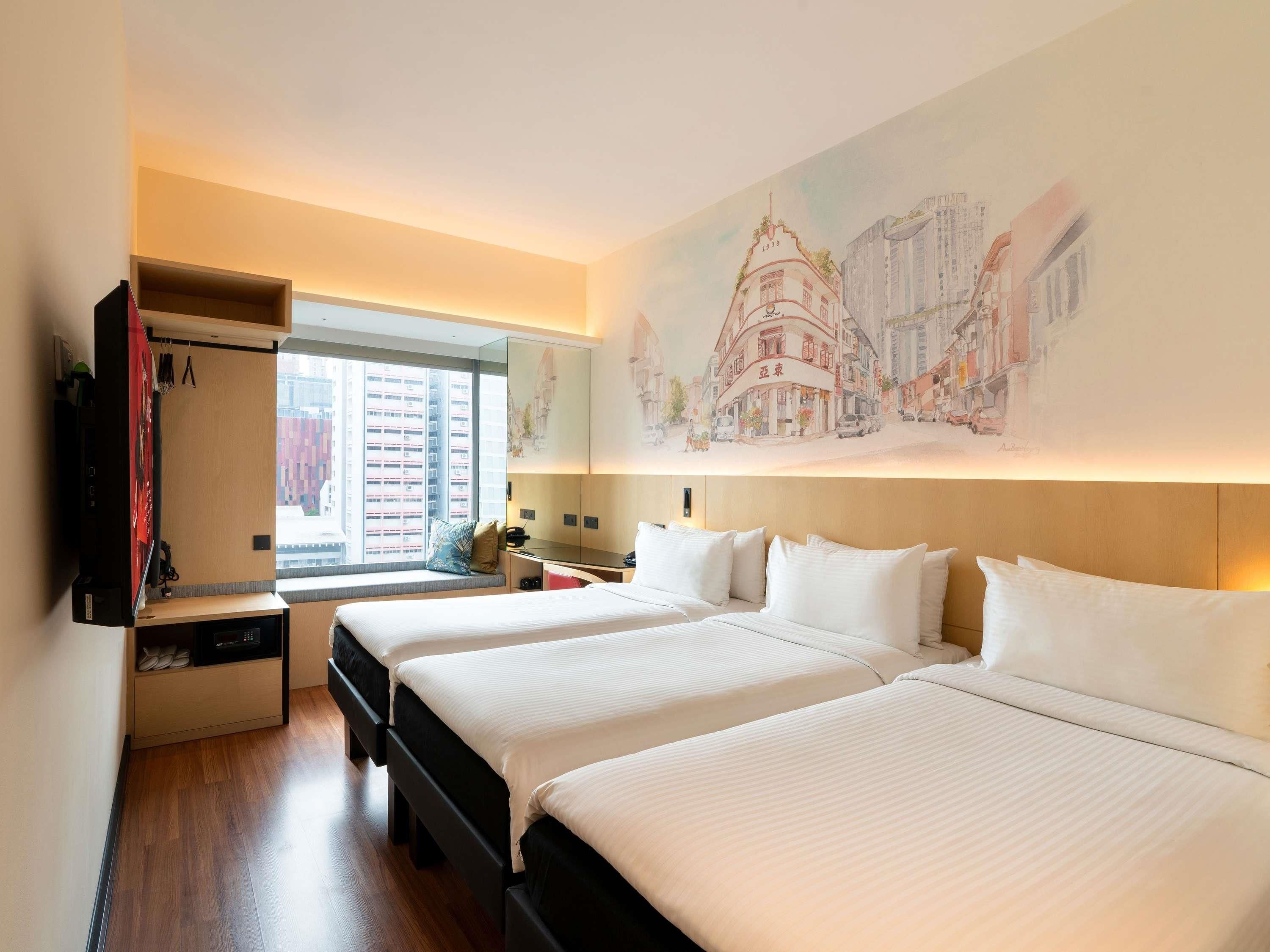 A hotel room with two beds, a TV, a desk, and a large window.