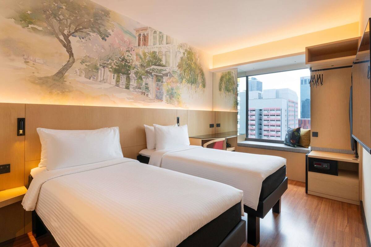 Een hotelkamer met twee bedden, een groot raam met uitzicht over de stad, een muurschildering en een kledingkast.