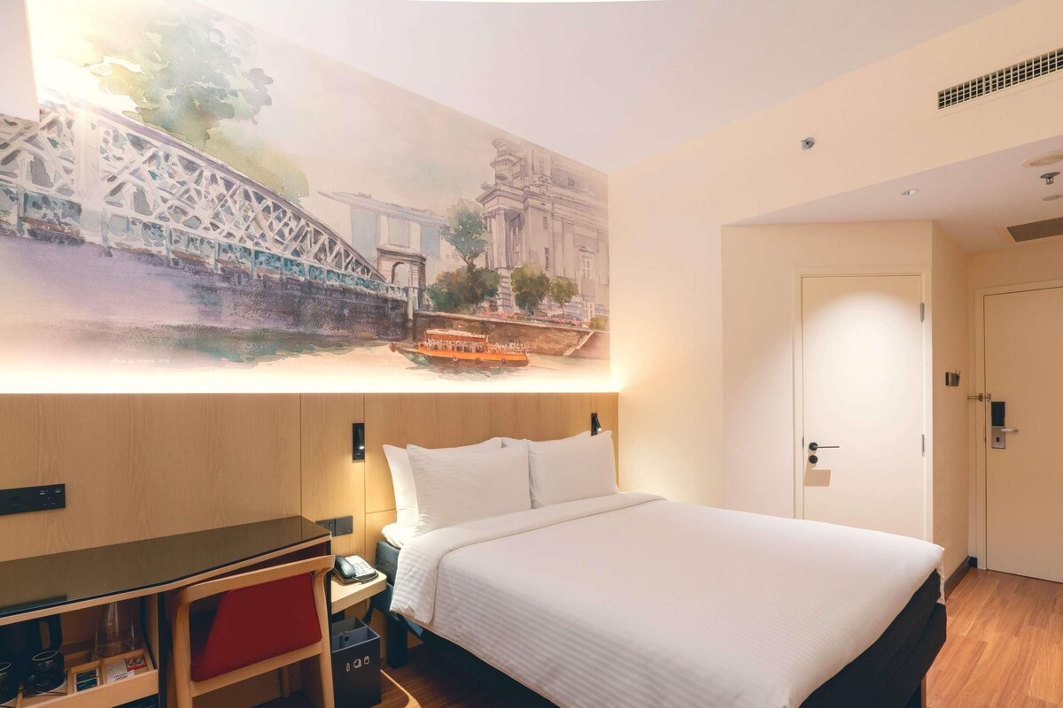 Een hotelkamer met een bed, nachtkastje en een schilderij van een brug.