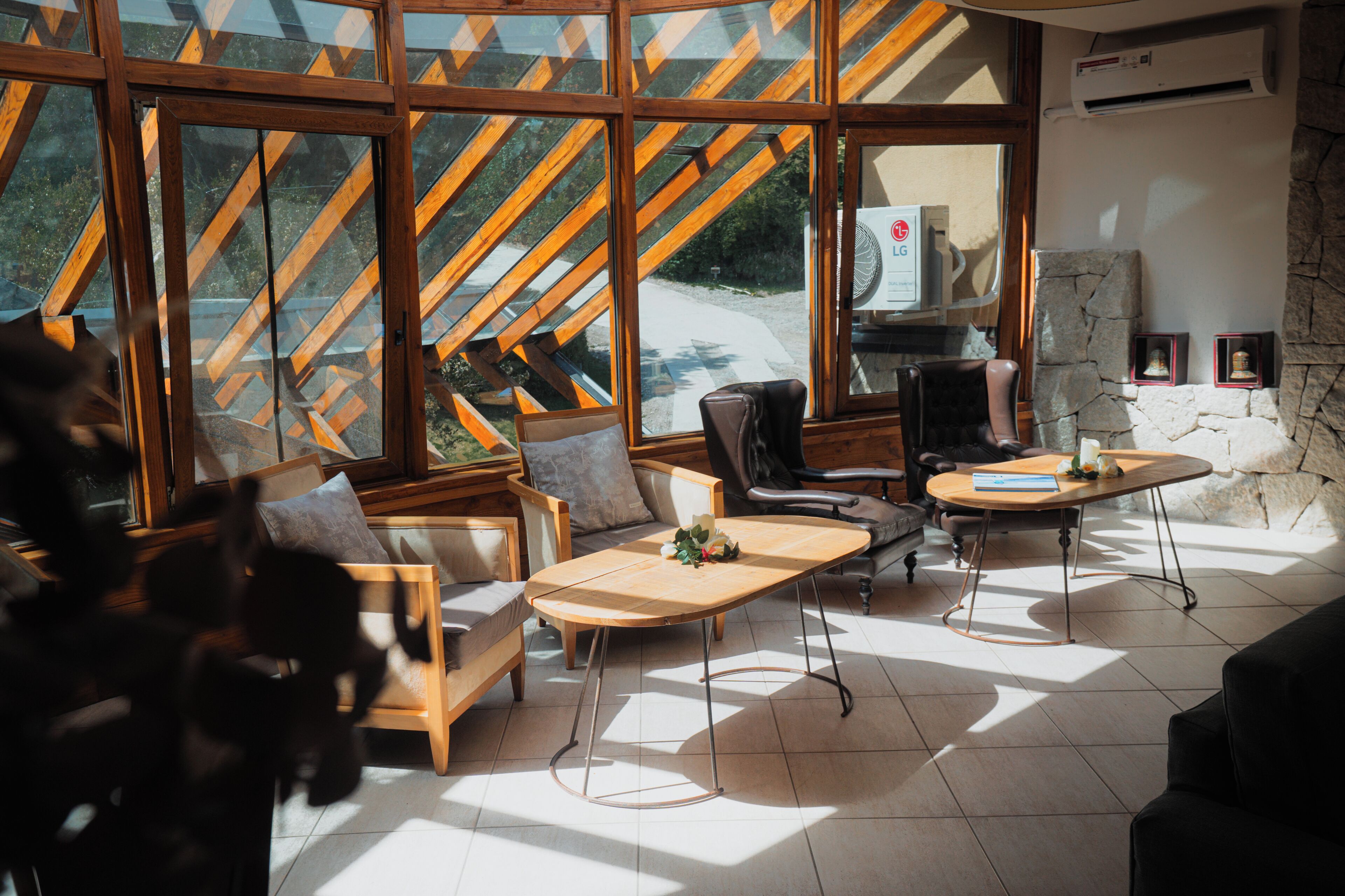 A modern interior with large windows, a stone wall, and a mix of wooden and leather furniture.