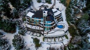 A multi-story building with a snow-covered roof and surrounding area, featuring a circular pool and multiple balconies. - Sol Arrayan Hotel & Spa (Villa La Angostura)