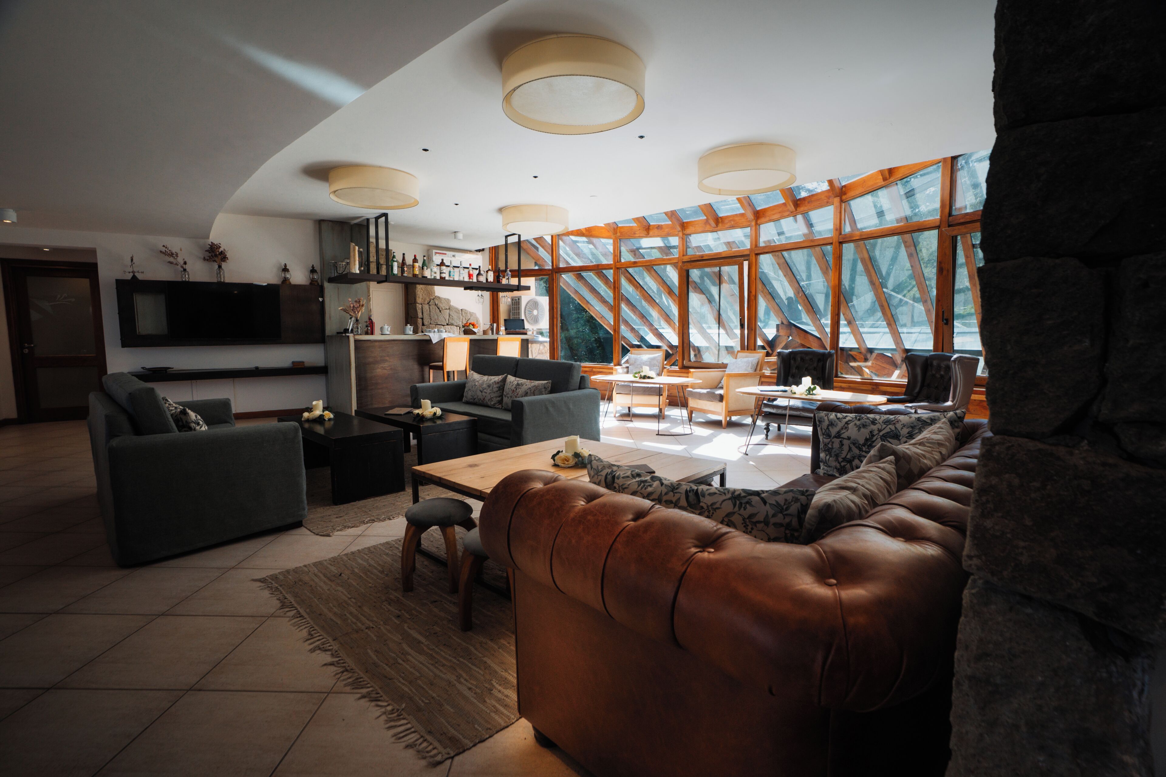 A modern living room with a leather sofa, a dining area, and a kitchen with a large window.