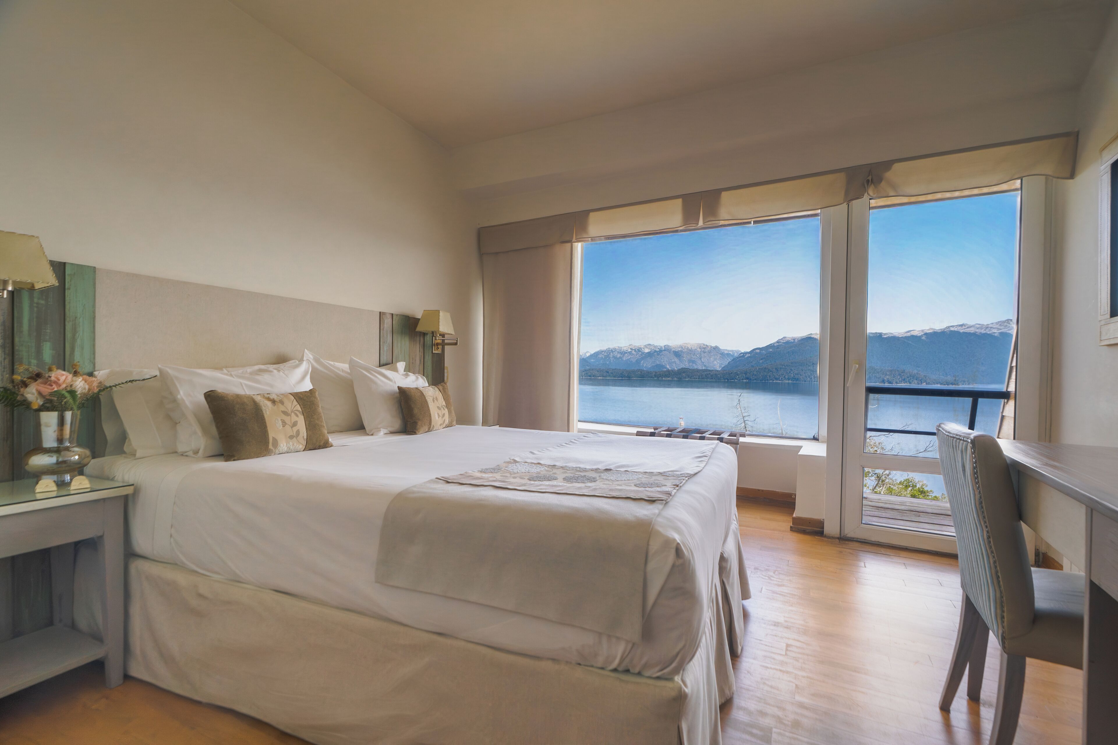 Un dormitorio con una cama grande, un escritorio y vistas a un lago y montañas.