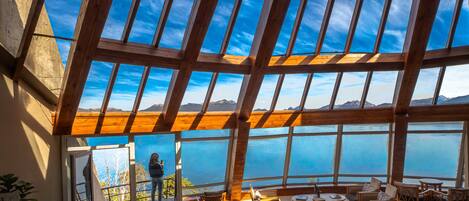 A spacious interior with a high ceiling and large windows offering a view of the sea and mountains.