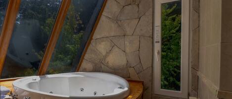 Un baño con pared de piedra, una bañera grande y un ventanal con vistas a árboles.