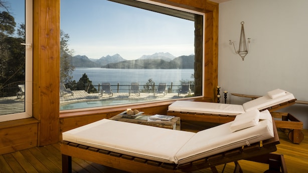 A room with two wooden beds, a large window overlooking a lake and mountains, and a small table with a candle and a book. - Sol Arrayan Hotel & Spa (Villa La Angostura)