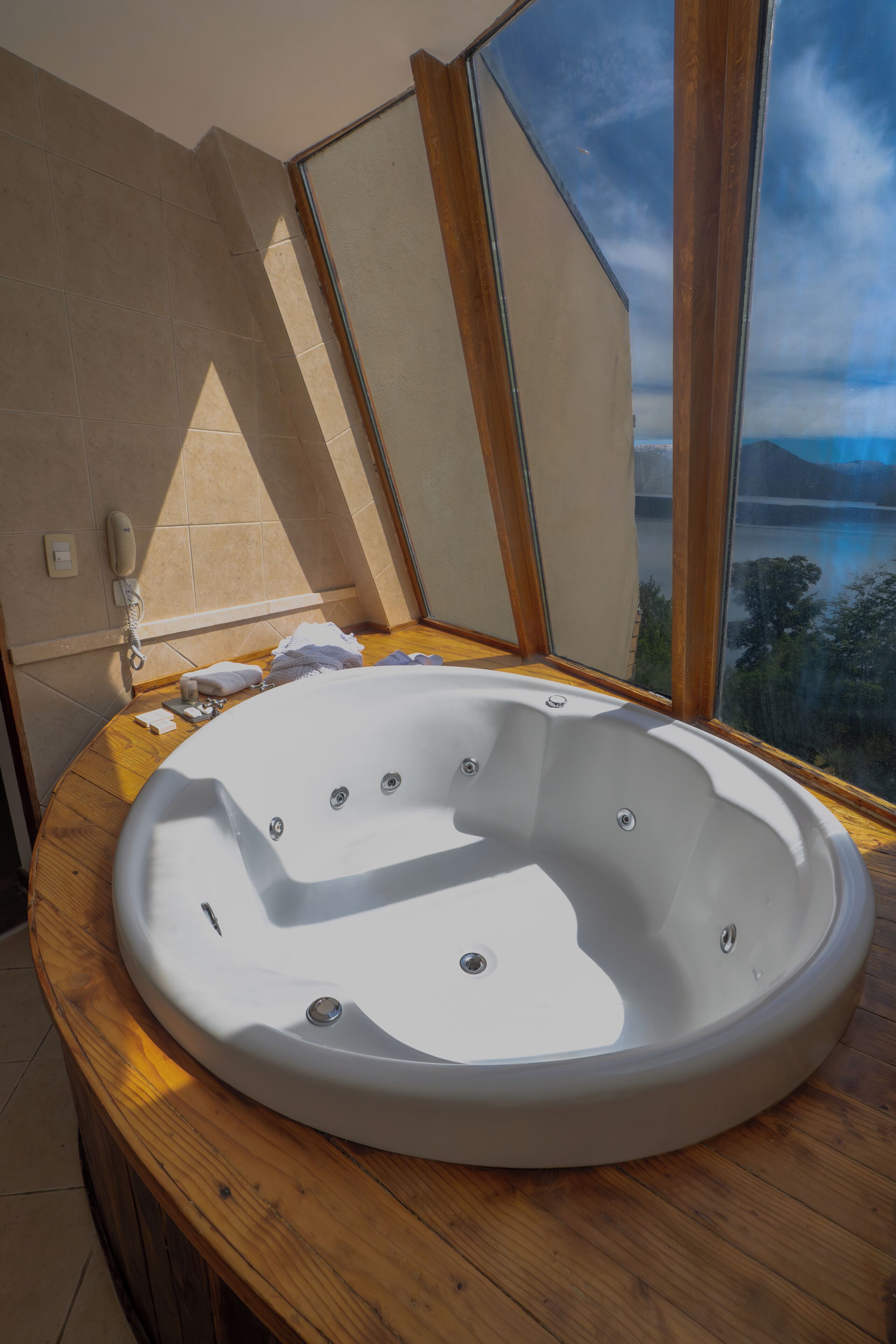 A bathroom with a large bathtub, a wooden vanity, and a view of a lake through a large window.