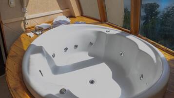 A bathroom with a large bathtub, a wooden vanity, and a view of a lake through a large window.
