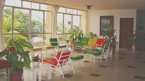 Un amplio espacio interior con ventanas grandes, sillas blancas y plantas en macetas.