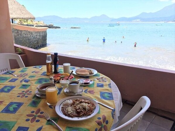 A dining table with breakfast items and a view of the sea and mountains.