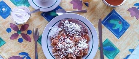 A table with a colorful tablecloth, a plate of enchiladas, a cup of coffee, a glass of orange juice, and a glass of red sauce.