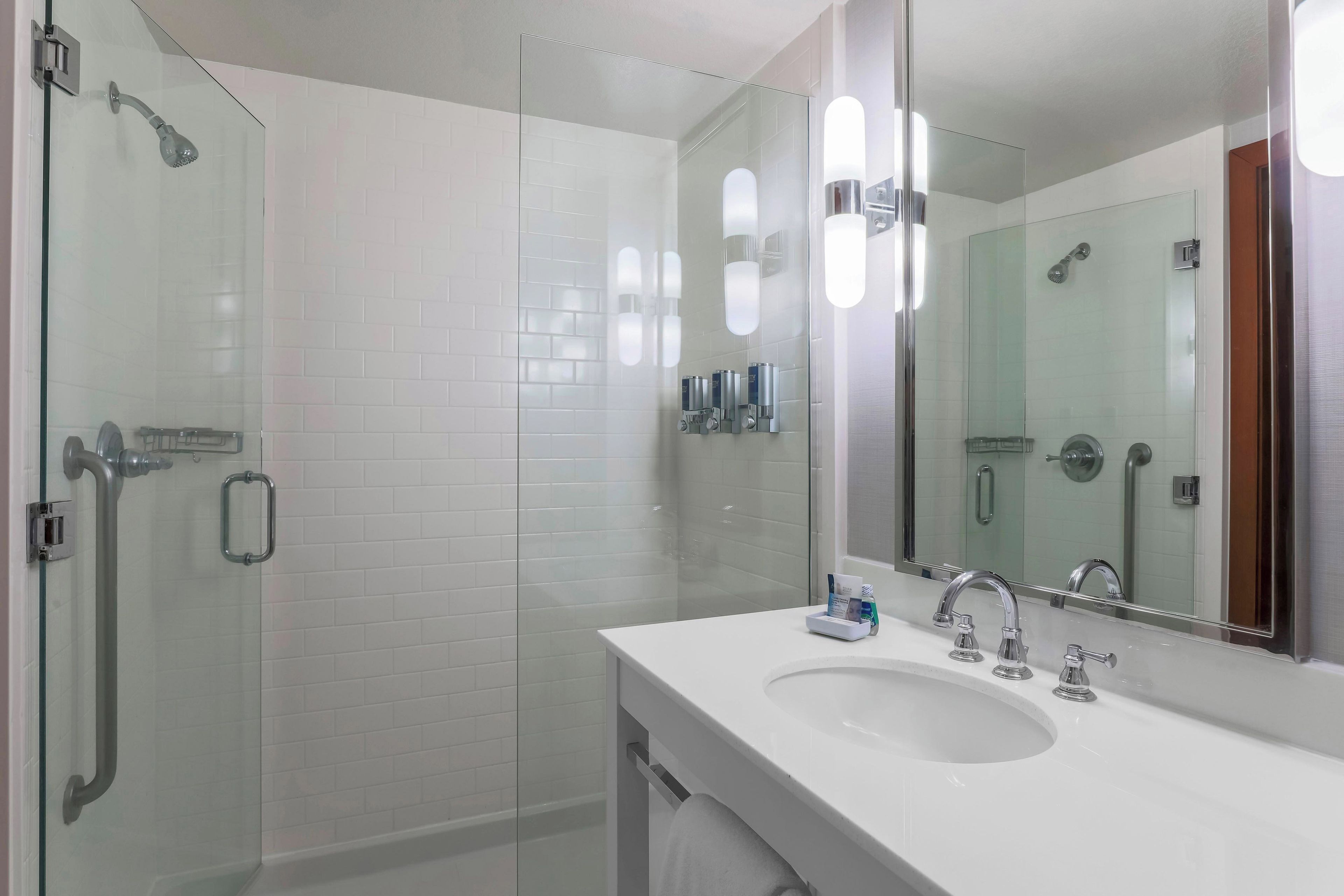 Une salle de bain moderne avec une douche à parois de verre, un lavabo blanc avec un miroir et un porte-serviettes.