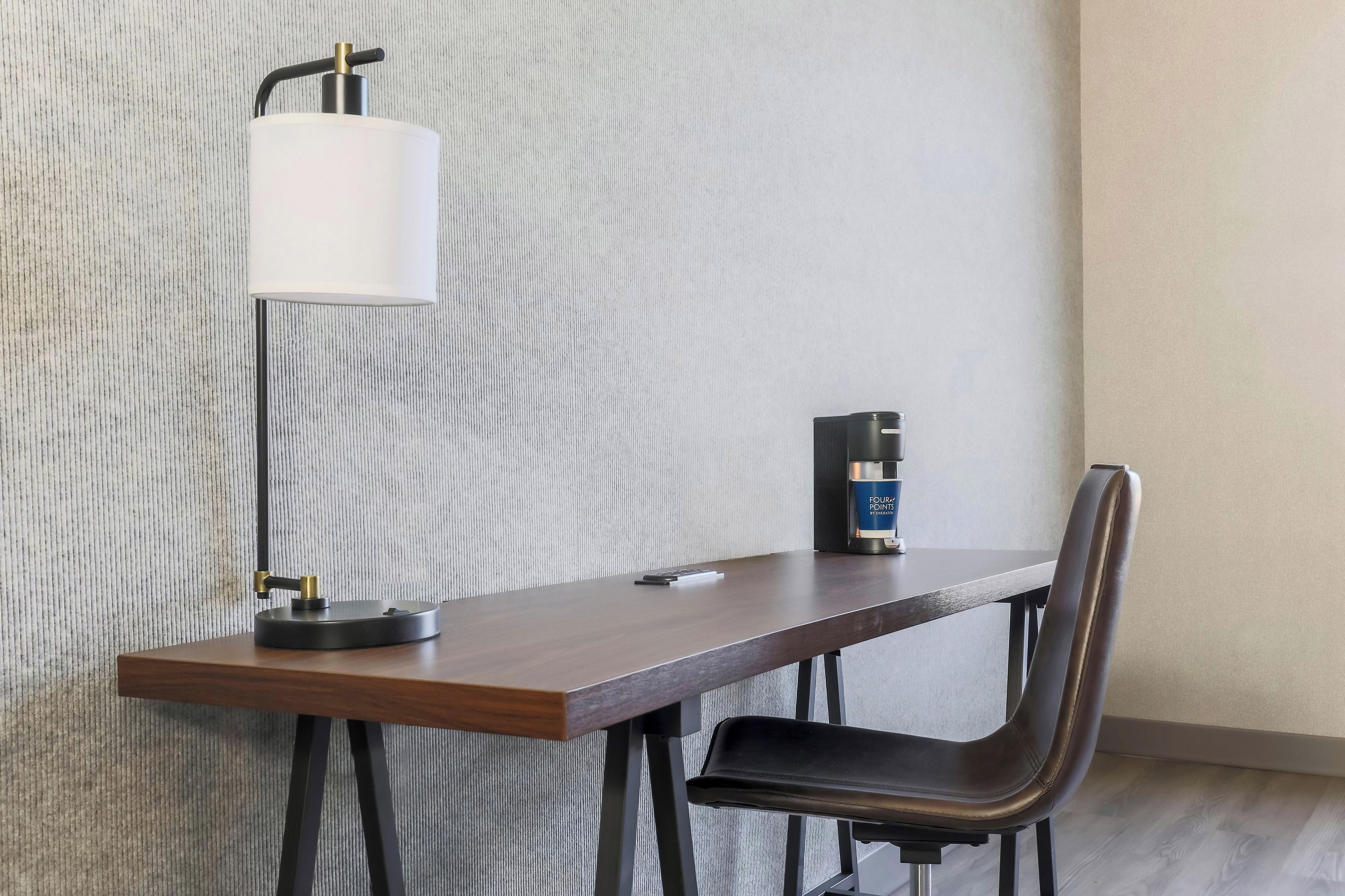Una habitación moderna con un escritorio de madera, una silla, una lámpara y una cafetera.