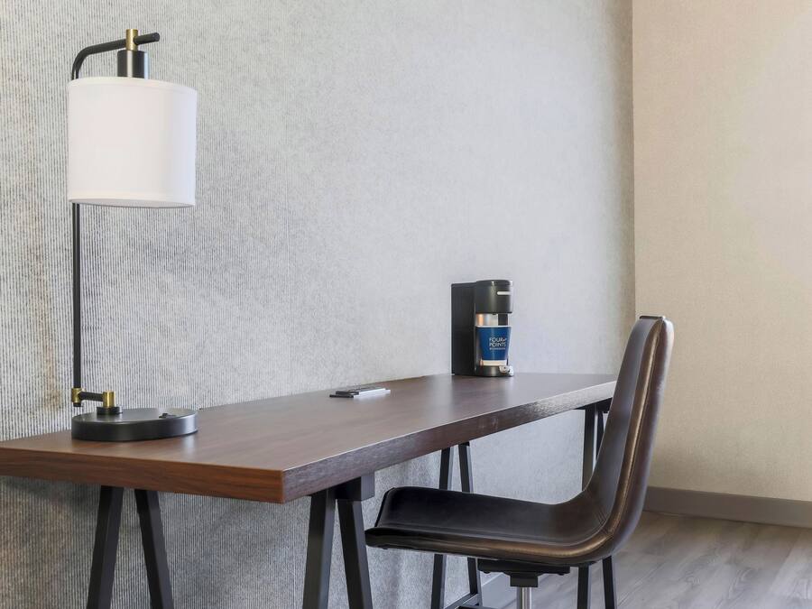 Una habitación moderna con un escritorio de madera, una silla, una lámpara y una cafetera.