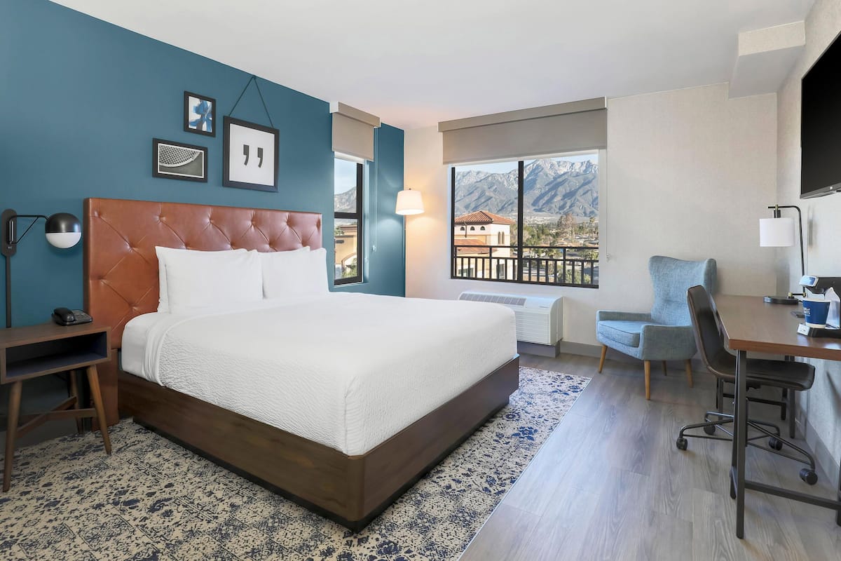 Ein Hotelzimmer mit einem großen Bett, einem Schreibtisch, einem Sessel und Bergblick.