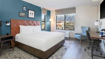 A hotel room with a bed, a desk, a chair, a window with a mountain view, and a TV.