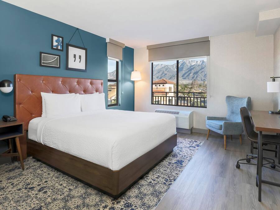 Ett hotellrum med en säng, ett skrivbord, en stol, ett fönster med utsikt över bergen och en tv.