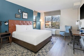 Een hotelkamer met een groot bed, een bureau, een stoel en uitzicht op bergen.