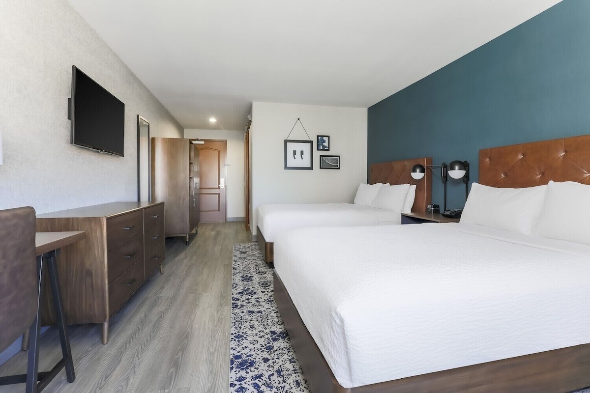 Hotelkamer met een groot bed, bureau, televisie en een badkamer zichtbaar door een geopende deur.