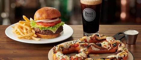A burger, fries, a pizza, and a glass of beer on a wooden table.