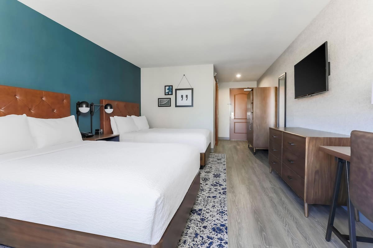 Ein Hotelzimmer mit zwei Betten, einem Schreibtisch, einem Fernseher und einem Kleiderschrank.