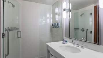 Un baño moderno con cabina de ducha de vidrio, un lavabo blanco con espejo y una puerta de cristal.