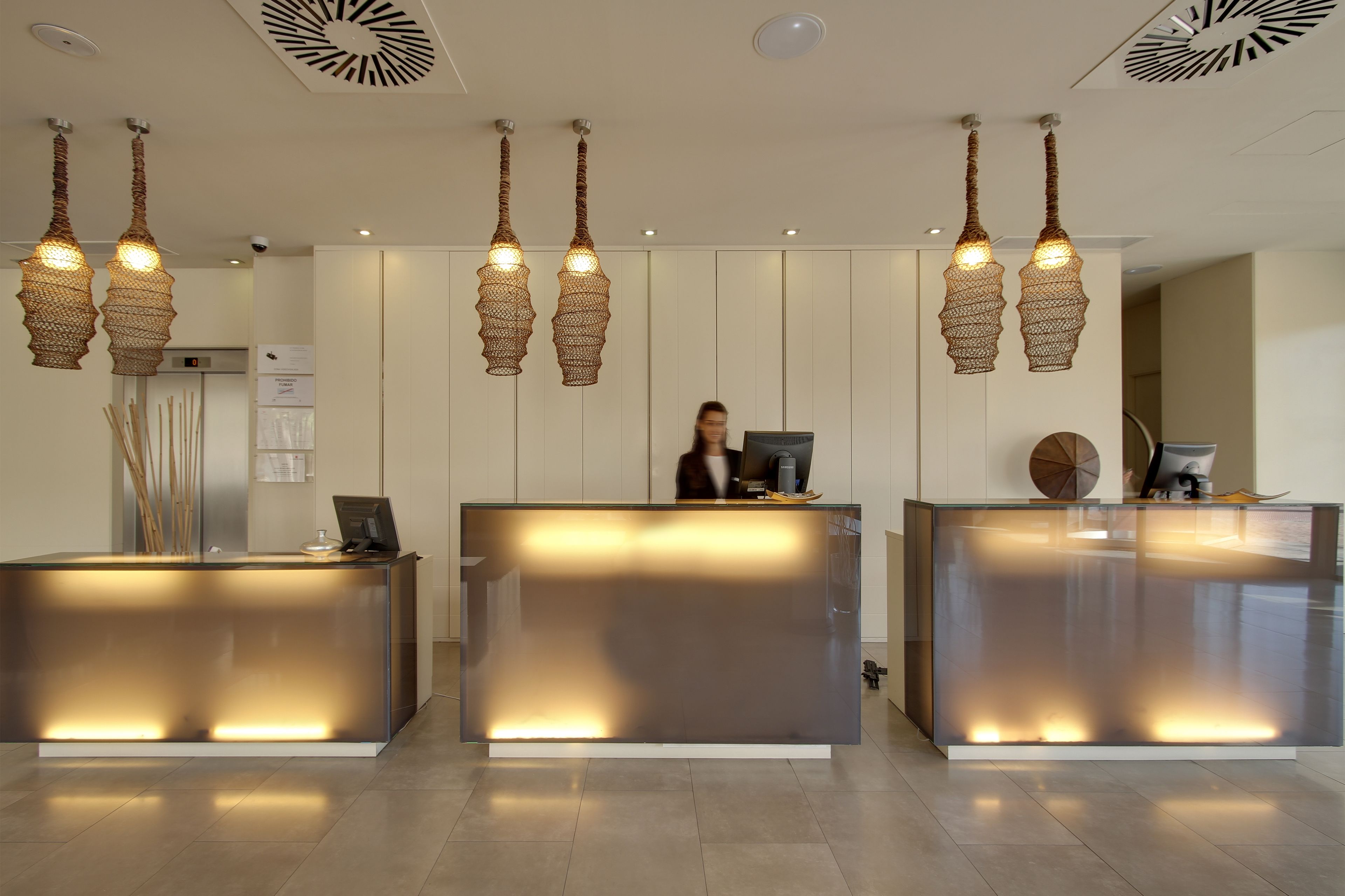 A reception area with three glass-fronted reception desks, each with a woven light fixture above.