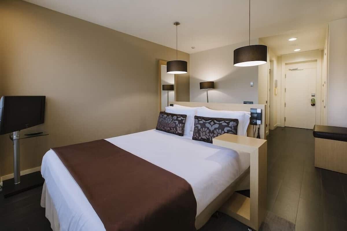 A hotel room with a bed, bedside tables, a TV, and a door.