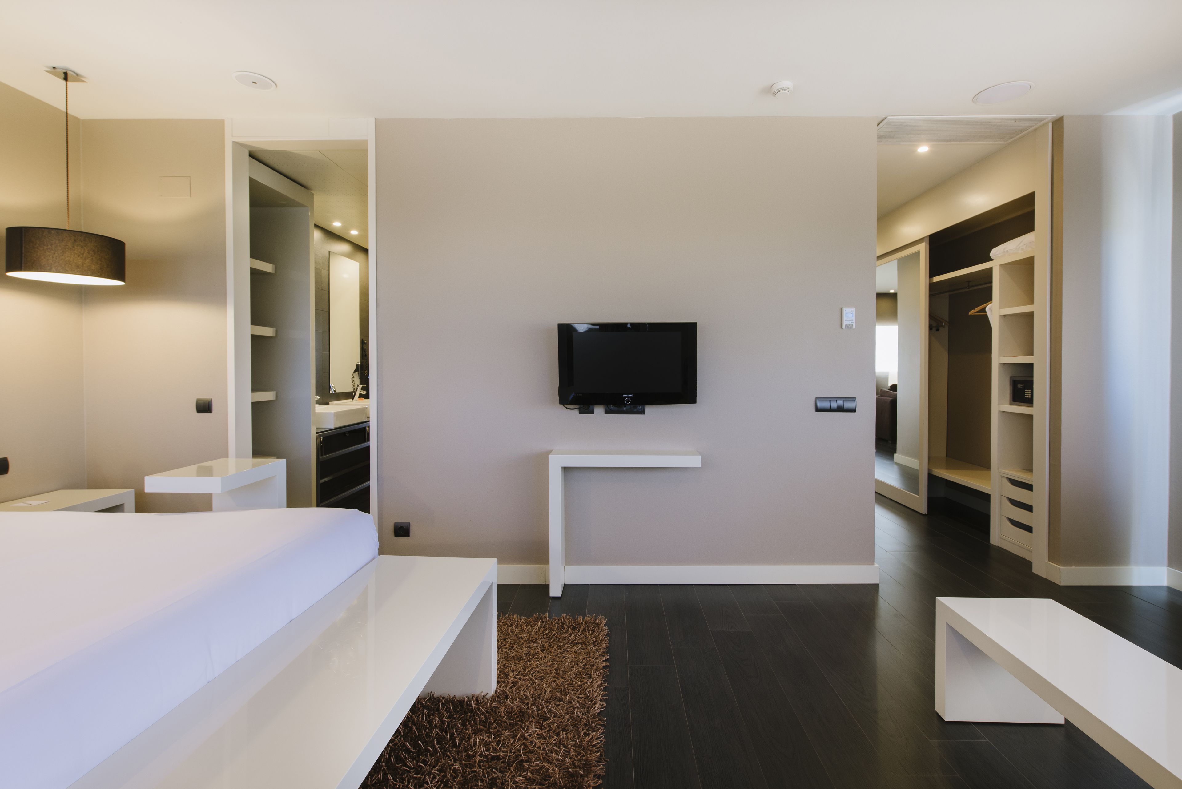 Una habitación de hotel moderna con una cama grande, un televisor en la pared y un vestidor.