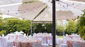An outdoor event space with multiple round tables set up under large umbrellas, each table equipped with white tablecloths, chairs, and glassware.