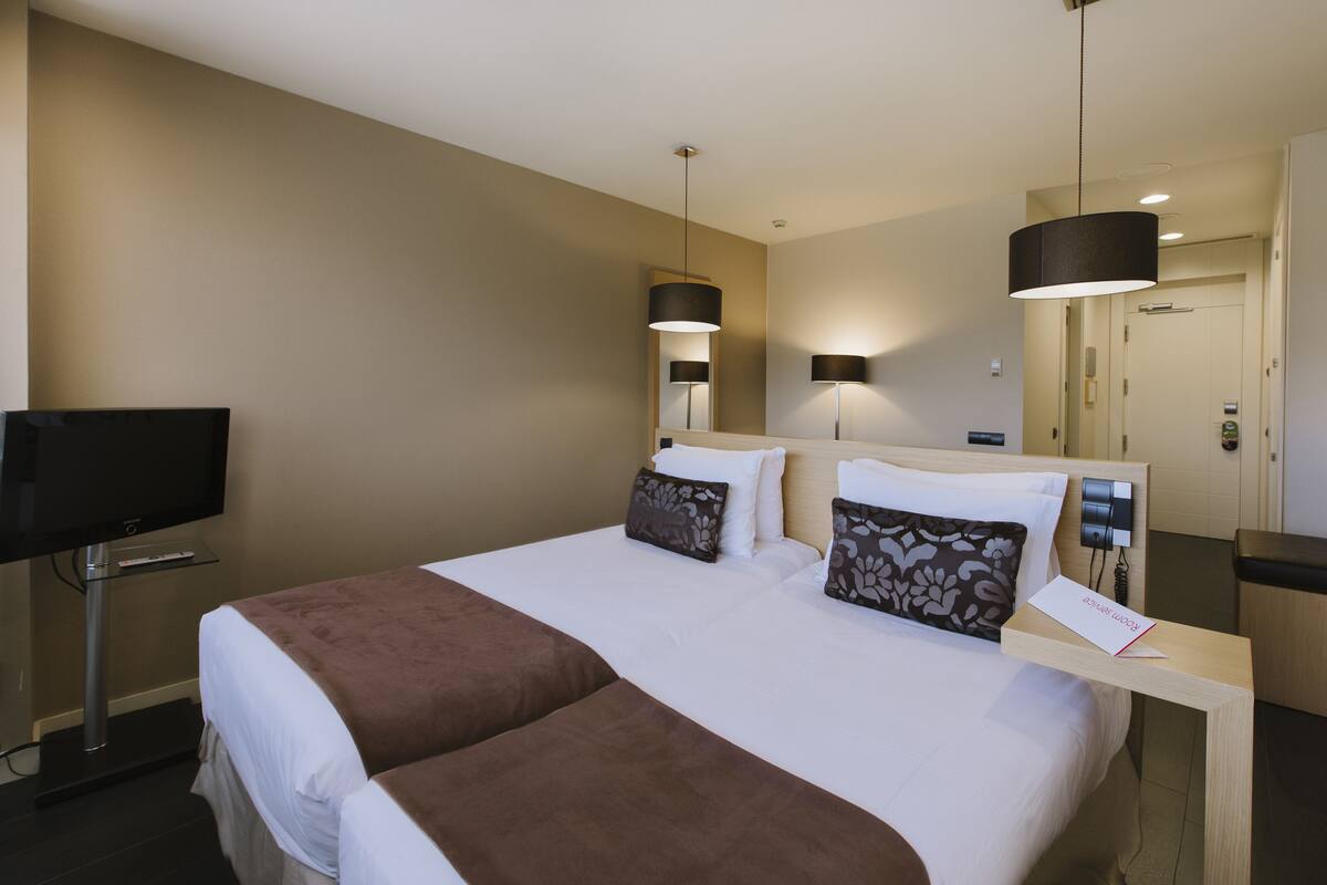 A hotel room with two beds, a TV, a desk, and a mirror.