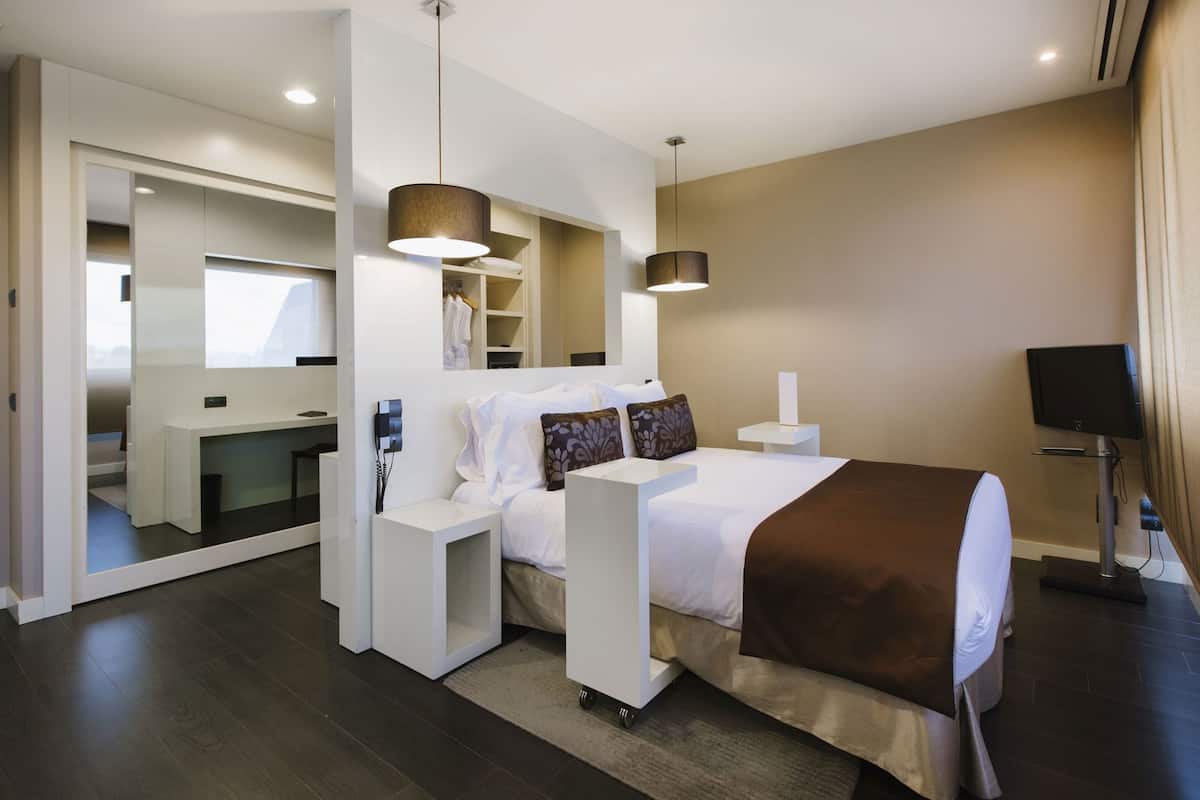 A modern hotel room with a large bed, bedside tables, a desk, and a television.