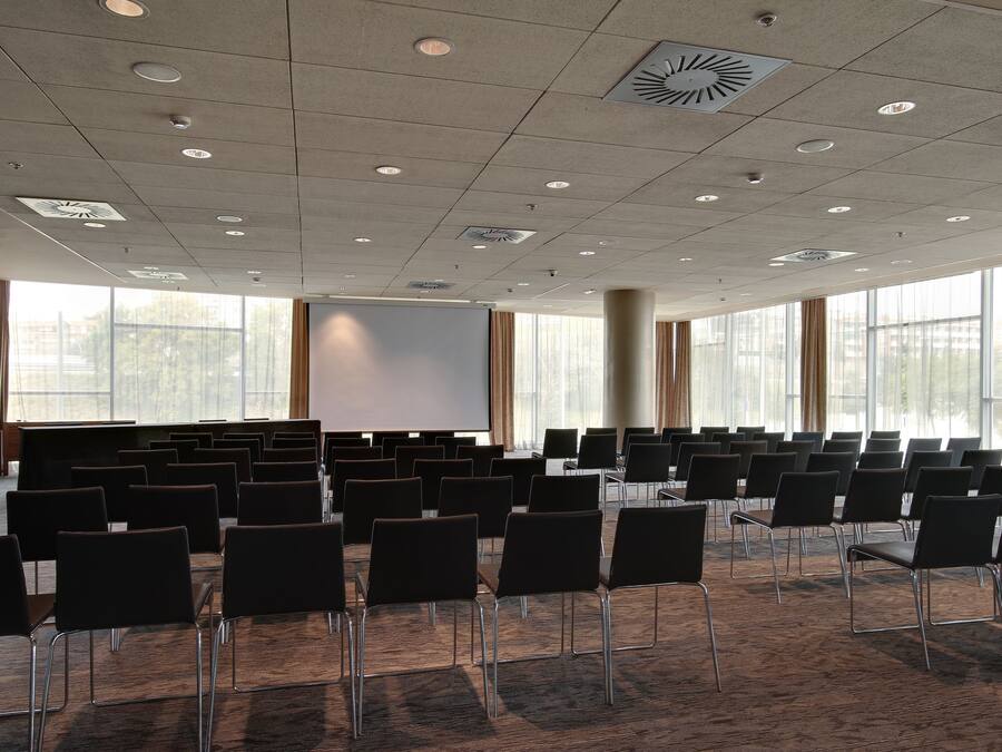 A conference room with rows of chairs, a projector screen, and large windows.